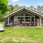 Haus mit Terrasse, Garten und Liegestühlen. Blick in Wohnbereich durch große Fenster.