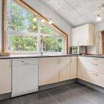 Küche mit Holzschränken, Spüle, Waschmaschine und Fenster zur Natur.