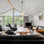 Wohnzimmer mit Sofa, Sesseln und TV. Große Fensterfront mit Blick auf Garten.