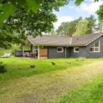 Ein graues Ferienhaus mit Terrasse und Garten unter Bäumen.