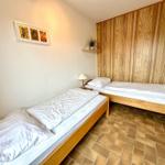 Zwei Betten mit weißen Laken, Holzwand und Fliesenboden.