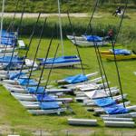 Mehrere Segelboote mit blauen Plane auf grünem Rasen.