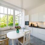 Küche mit Esstisch, großen Fenstern und weißen Schränken.