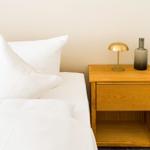 Ein Bett mit weißen Kissen und einer Nachttischlampe neben einem Holznachttisch.