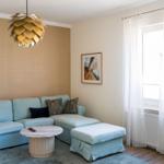 Ein Wohnzimmer mit Sofa, Couchtisch und Fenster. Deckenleuchte und Wandbild sind sichtbar.