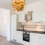 Küche mit weißen Schränken, Edelstahlspüle und moderner Deckenleuchte.