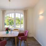 Esszimmer mit Tisch, Stühlen und großem Fenster. Blick auf grüne Bäume.