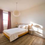 Schlafzimmer mit Bett, Fenster, Lampe und dekorativem Schrank.