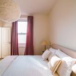 Schlafzimmer mit Bett, Fenster, Vorhängen und Deckenleuchte.