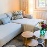 Ein Sofa mit Kissen und zwei runden Tischen. Ein Fenster und ein Heizkörper sind sichtbar.