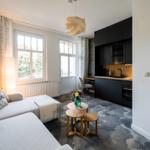 Wohnbereich mit Sofa, Tisch und Küchenzeile. Fenster mit Blick auf Balkon.