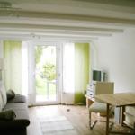 Wohnraum mit Sofa, Tisch und TV. Durchgang zur Terrasse mit Blick auf Garten.