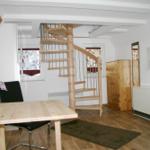 Raum mit Holztreppe, Tisch, Stuhl und Kleiderschrank. Fenster mit Vorhängen.