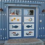 Eingangstür mit Fisch- und Ankerdekoration. Blaue Holzwand mit weißen Streifen.