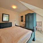 Schlafzimmer mit Bett, Kleiderschrank und Stuhl unter schrägem Dach.