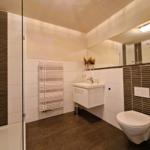 Badezimmer mit Dusche, Waschbecken und Toilette. Weiße Fliesen und dunkle Bodenfliesen.