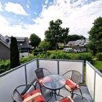 Terrasse mit Tisch und vier Stühlen, Blick auf Grünanlagen und Häuser.