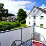 Terrasse mit Tisch und Stühlen. Blick auf grüne Wiese und Haus mit Streifenfassade.