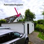 Fahrradschuppen mit Eingang und Dach. Hintergrund: Haus mit Dachfenstern.