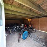 Holzüberdachter Fahrradstellplatz mit mehreren Fahrrädern und einem Fahrradständer.