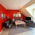 Wohnzimmer mit roten Wänden, Sofa, zwei Sessel und Fernseher.