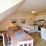 Essbereich mit Tisch und Stühlen, Küche mit weißen Schränken und Kacheln an der Wand.