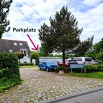 Parkplatz vor einem Haus mit Bäumen und gepflastertem Weg.