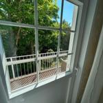 Blick aus dem Fenster auf Balkon mit Geländer und grüne Bäume.