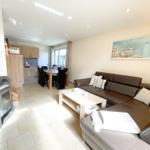 Wohnzimmer mit Sofa, Esstisch und Holzküche. Holzofen und Wandbild sichtbar.