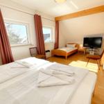 Zimmer mit Doppelbett, Einzelbett, TV und Holzboden.