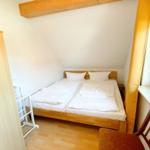 Zimmer mit Doppelbett, Kleiderschrank und Fenster. Holzboden und Deckenbalken.