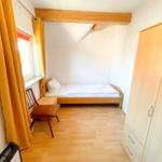 Ein Schlafzimmer mit einem Bett, einem Kleiderschrank und einem Stuhl vor einem Fenster.