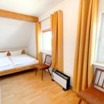 Doppelbettzimmer mit Holzboden, zwei Stühlen und Fenstern mit Vorhängen.