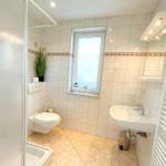 Badezimmer mit Toilette, Waschbecken und Fenster. Duschbereich mit Dusche.