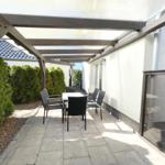 Terrasse mit Tisch und Stühlen unter Dach, umgeben von Hecken und Wand.