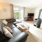 Wohnzimmer mit Ledersofa, Kaminofen und TV. Durchgang zur Terrasse.