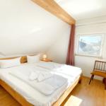 Doppelbett mit weißen Laken, Holzmöbel und Fenster mit Vorhängen.