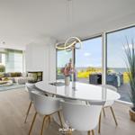 Essbereich mit weißem Tisch und Stühlen. Große Fenster zeigen Blick aufs Wasser.