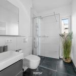 Bad mit Dusche, Waschbecken und Toilette. Dunkler Boden und Pflanze.