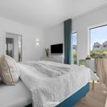 Schlafzimmer mit Bett, Fernseher und großem Fenster mit Blick auf die Außenanlage.