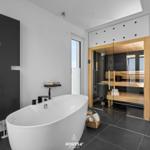 Bad mit freistehender Badewanne und Sauna mit Glaswand.