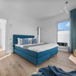 Schlafzimmer mit blauem Bett, Holzboden und großem Fenster mit Blick.