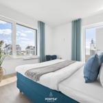 Schlafzimmer mit großem Fenster, Bett und Pflanze.