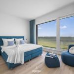 Schlafzimmer mit Blick aufs Wasser, blaues Bett und Sessel.