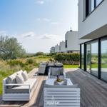 Terrasse mit Sitzgruppe und Tisch. Blick auf Grünfläche und moderne Häuser.