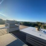Terrasse mit weißem Tisch und Stuhl, Sonne, Blick auf Wasser und Gras.