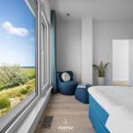 Schlafzimmer mit Blick auf Grasland und Meer. Blaue Sitzgelegenheit und Bett.