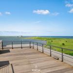 Terrasse mit Blick auf Wasser und Grünland unter blauem Himmel.
