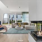 Wohnzimmer mit Kamin, Sofa und Sessel. Durchgang zur Terrasse.