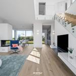 Wohn- und Essbereich mit Kamin, TV und Holztreppe. Durchgehendes Glasgeländer und großflächige Fenster.